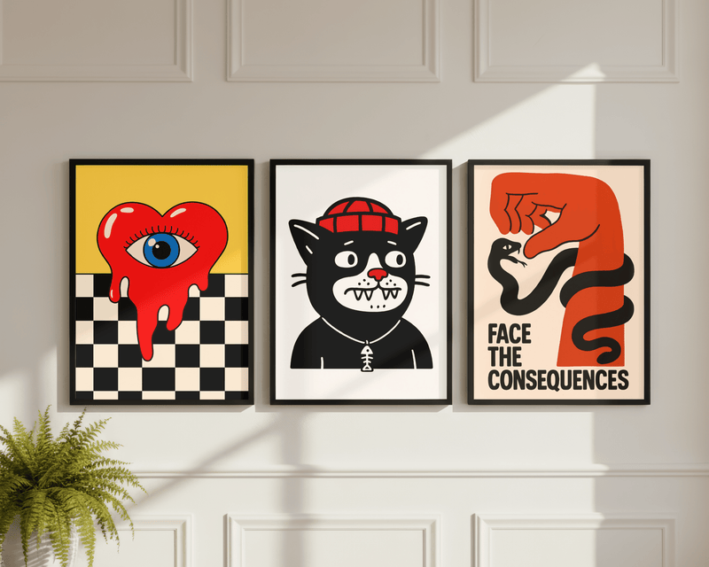 Drei gerahmte Poster der offbeat Collection an einer Wand – buntes Pop-Art-Herz mit Auge, schwarze Katze mit Beanie und „Face The Consequences" Schlangen-Motiv in Schwarz-Rot